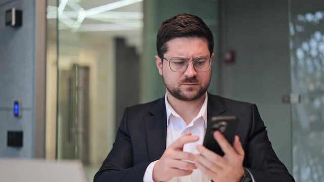 Business professional appears confused while interacting with mobile phone. Moments of frustration and perplexity are evident during problem-solving. Shows modern connectivity challenges in workspace.