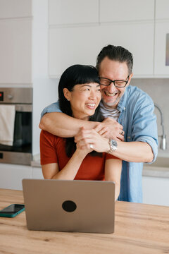 Smiling couple hugging in kitchen using laptop together