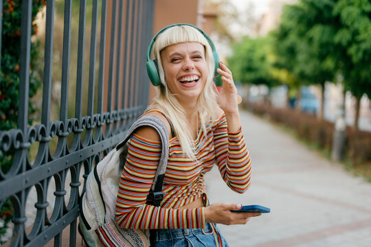Happy woman enjoying music with headphones on urban sidewalk