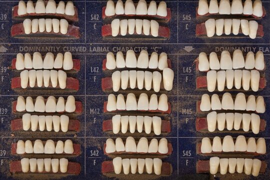Close up view of rows of replacement teeth on a worn shade board in an old time dentist office, showing varied sizes and shades with a dusty vintage look and dental history feel.