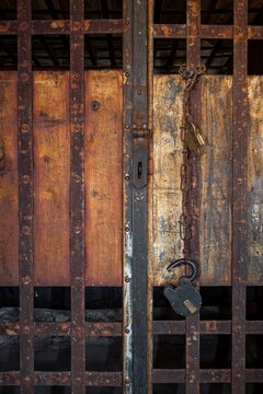 Close view of a frontier jail door with rusty iron bars, chain, and padlock against weathered wood
