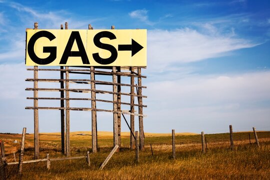 Large roadside GAS arrow sign on a weathered wooden billboard stands in a rural prairie under a blue sky, suggesting fuel ahead, travel, and open road vibes in the Great Plains, South Dakota