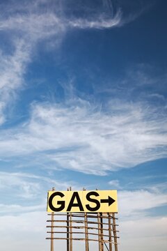 Large roadside GAS arrow sign on a weathered wooden billboard stands in a rural prairie under a blue sky, suggesting fuel ahead, travel, and open road vibes in the Great Plains, South Dakota
