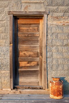 A rustic wooden door and old milk can catch warm evening light on a prairie building in South Dakota, showing rich texture, patina, and the charm of rural homestead life.