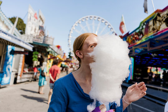 Happy woman smiling and hiding behind cotton candy at colorful fair