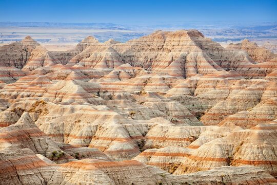 Panoramic view of striped buttes and eroded hills at a scenic overlook in Badlands National Park, South Dakota, under a clear blue sky.