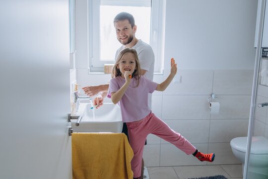 Father and daughter brushing teeth together in bathroom during morning routine