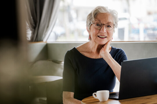 Senior woman using laptop and enjoying coffee at caf� with positive attitude