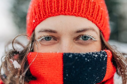 Winter portrait of a woman with frozen eyelashes and red knit hat outdoors