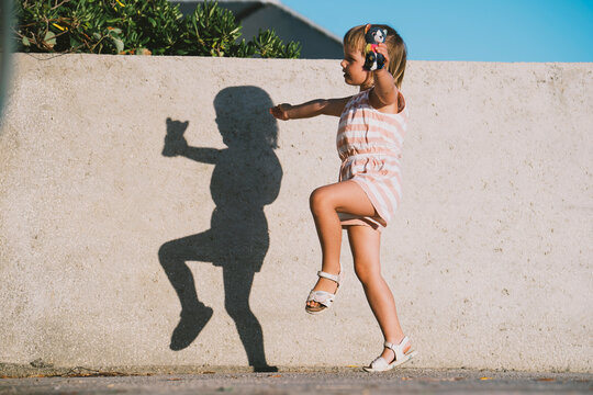 Child playing and dancing outdoors casting a shadow on sunny day