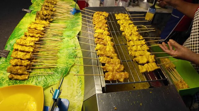 Thai Street Food Vendor Brushing Chicken Satay Skewers on Grill
