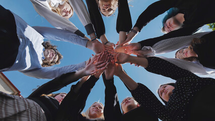 Students joining hands together in a circle, symbolizing unity and teamwork on a bright school day © Довидович Михаил