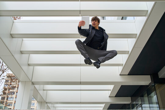 Man jumping mid-air taking selfie in modern urban environment