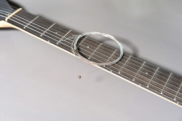 Close-up of a guitar neck with dark fretboard, metal frets, dot inlays, and a coiled set of new metallic strings resting across the frets.