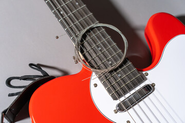 Close-up of a red electric guitar with white pickguard, dark fretboard, metal frets, dot inlays, and a coiled set of new metallic strings resting across the neck and body.