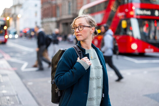 Woman with backpack commuting on busy city street near red bus