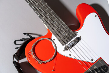 Close-up of a red electric guitar with white pickguard, dark fretboard, metal frets, dot inlays, black strap, and a coiled set of new metallic strings resting on the body.