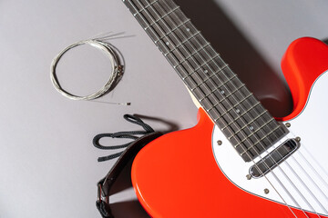 Close-up of a red electric guitar with white pickguard, dark fretboard, metal frets, dot inlays, coiled replacement strings, and a black strap with a leather end placed beside the neck.