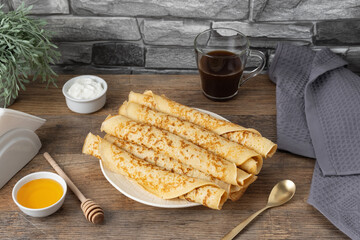 Stack of rolled pancakes with honey, yogurt, and coffee on a table with stone wall background