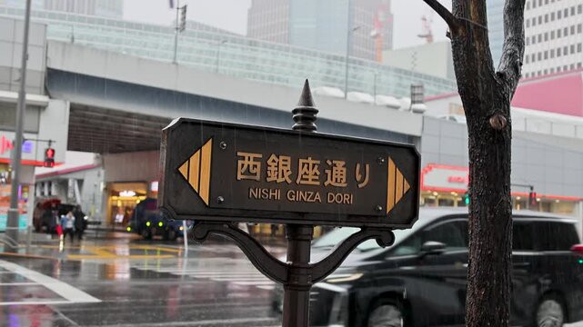 Nishi Ginza Dori street sign in rain near busy intersection in Tokyo Japan