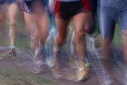Energetic motion blur of runners sprinting on dirt path, dynamic action and speed in outdoor race event. Grain and texture of 35mm film scan. 