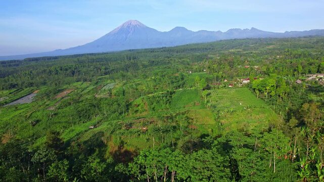 Aerial drone footage of a vast green wild valley nearby the main road leading to B29 summit in Bromo, with Semeru high volcano behind, in Senduro area, Lumajang regency, Java island, Indonesia