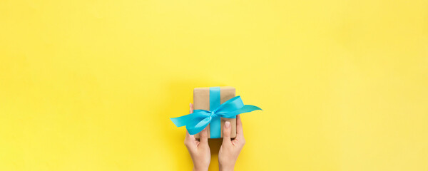 Fototapeta premium Woman arms holding gift box with blue ribbon on color background, top view