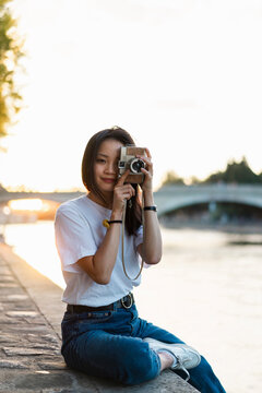 France, Paris, portrait of young woman with camera at river Seine at sunset