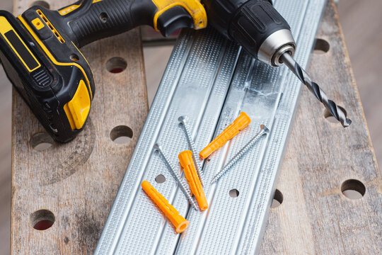 Cordless drill with drill bit, plastic wall plugs and metal screws on galvanized metal profile. Construction and installation concept for renovation, drywall mounting and home improvement projects.