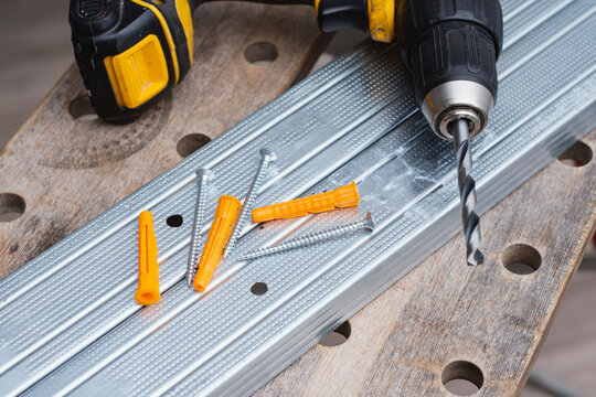 Cordless drill with drill bit, plastic wall plugs and metal screws on galvanized metal profile. Construction and installation concept for renovation, drywall mounting and home improvement projects.