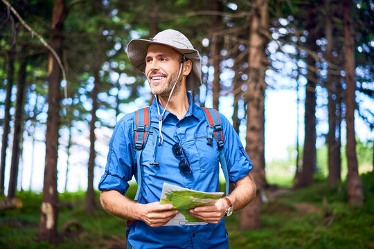 Smiling man holding a map hiking in the forest
