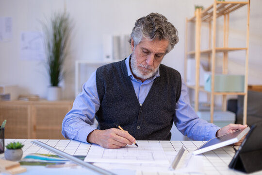 Architect drawing plans at desk with tablet in modern office