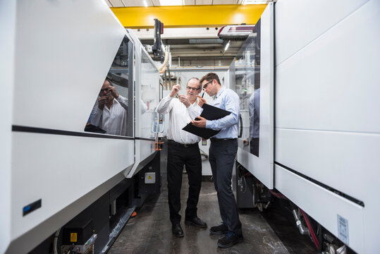 Two men talking among machines in factory shop floor