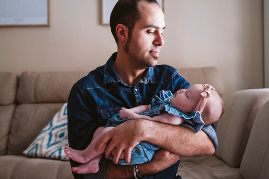 Father carrying sleeping baby girl on sofa at home