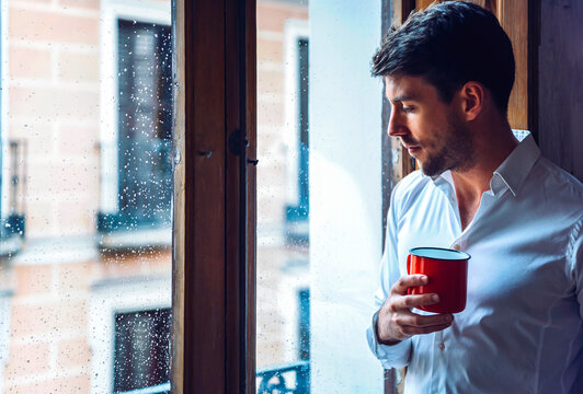 Young man holding cup looking out of window