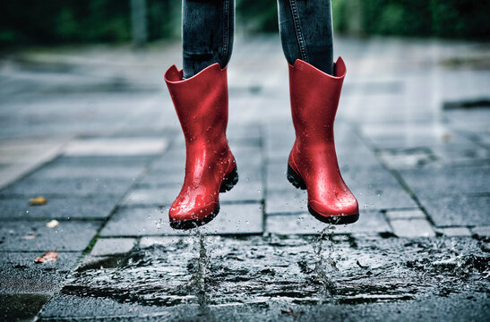 Feet of little girl wearing rubber boots jumping over small puddle
