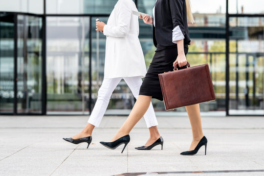 Businesswoman with briefcase using mobile phone while walking by colleague on footpath