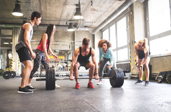 Group of young fit people cheering at man weightlifting in gym