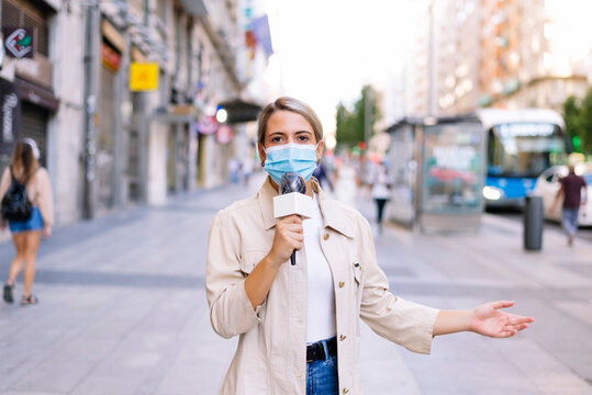 Female reporter wearing mask talking over microphone on street in city