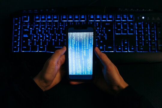 Computer hacker hand holding mobile phone against computer keyboard at office