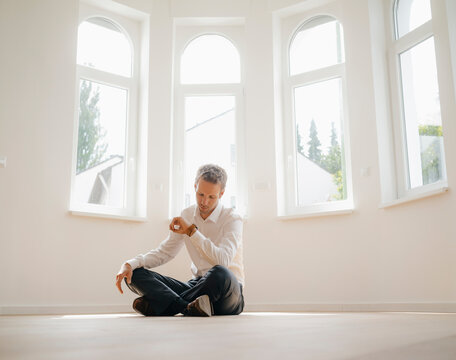 Businessman sitting on ground of his newly refurbished home, checking time