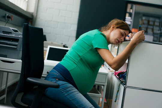 Exhausted pregnant woman sitting at desk in office