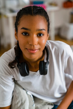 Smiling teenage girl with headphone around neck sitting in bedroom at home