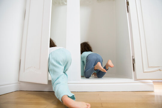 Two twin brothers crawling into wardrobe at home
