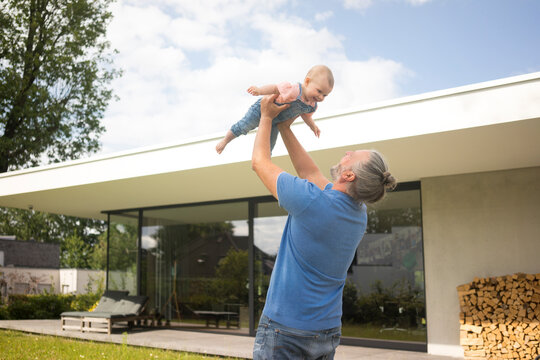 Happy mature man lifting up baby girl in garden of his house