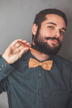 Man combing his beard with a wooden brush, wearing denim shirt and cork bow tie
