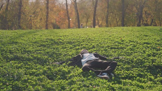 Man lying in open meadow, wide shot shows clover expanse and autumn trees, casual jacketed commuter taking restorative break, golden light and slow pan, cinematic serene atmosphere