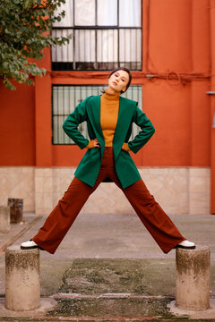 Young woman wearing green jacket standing on bollards against building in city