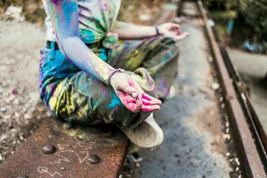 Girl with Holi colours on her clothes sitting on bridge, meditationg, Germany