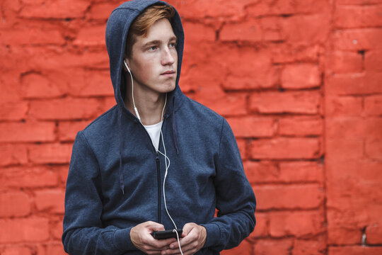Young man with cell phone and earphones at red brick wall